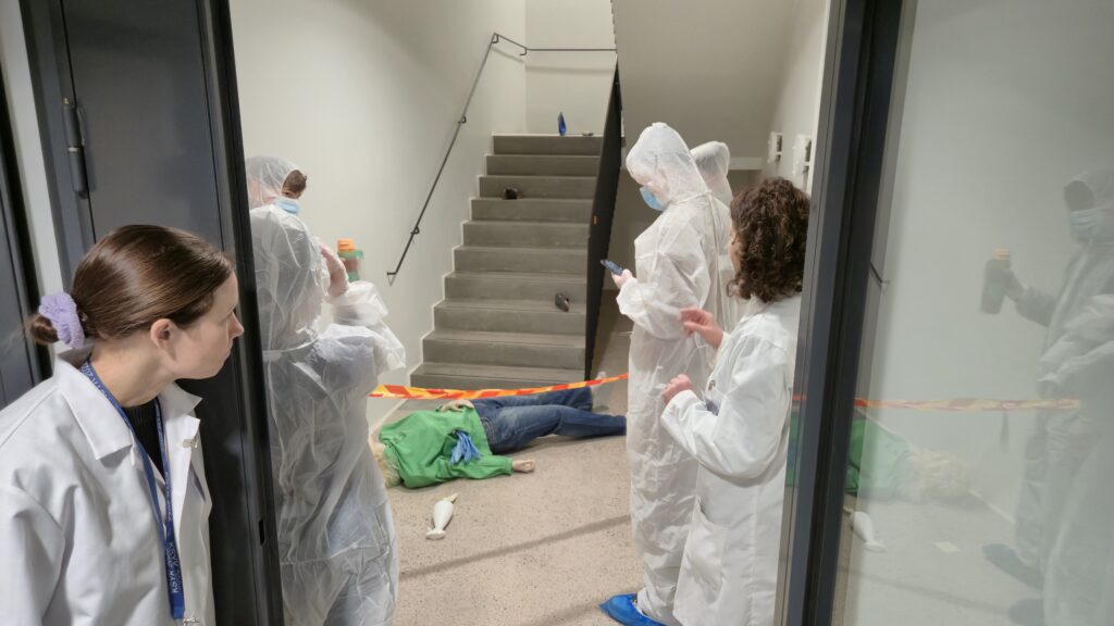 Rikostekninen tutkimus:
Opiskelijat tutkimassa rikospaikkaa valkoiset suojapuvut
 yllään. 
