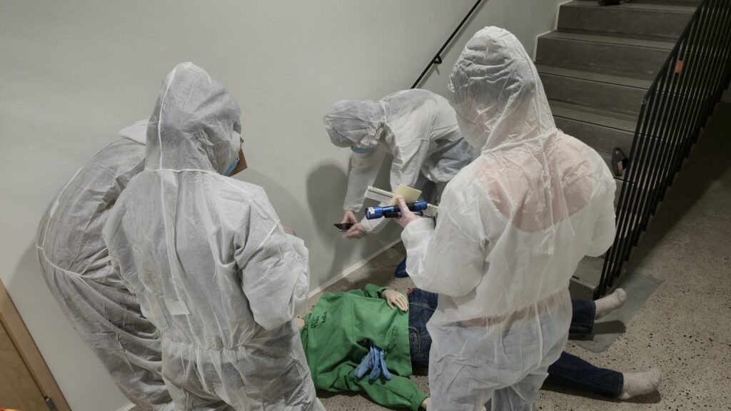 Rikostekninen tutkimus: Opiskelijat ovat tutkimassa rikospaikkaa valkoiset suojapuvut yllään.