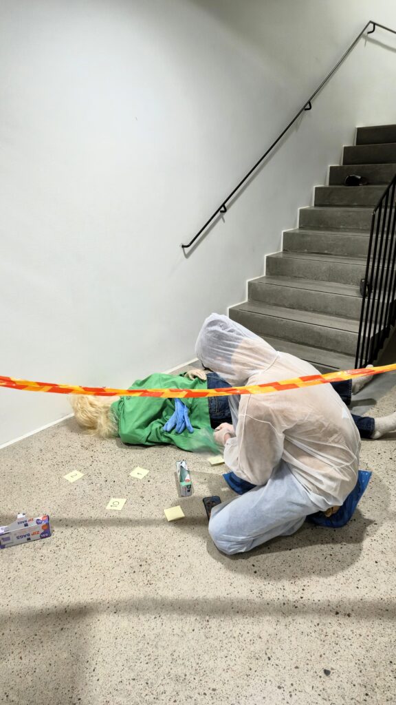 Rikostekninen tutkimus:
Opiskelija tutkimassa rikospaikkaa valkoinen suojapuku yllään.  

