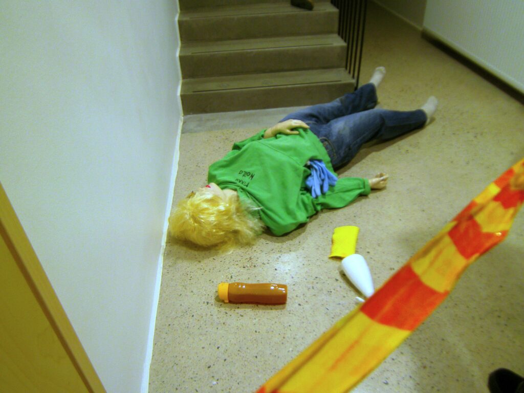 Rikostekninen tutkimus:
Näkymä rikospaikalta portaikon alaosasta: Portaikon alaosassa
makaa uhri, ympärillään todistusaineistoa sekä poliisin suojanauha. 
